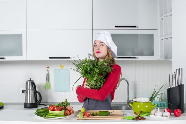 Front view female chef in cook hat holding up greens