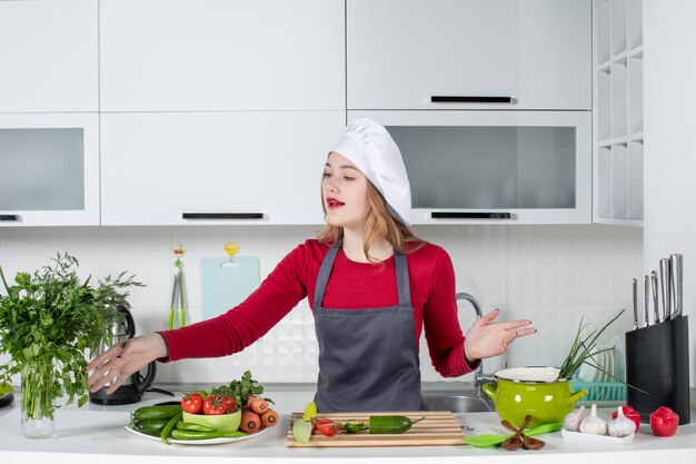 Front view female chef in cook hat reaching hand to greens