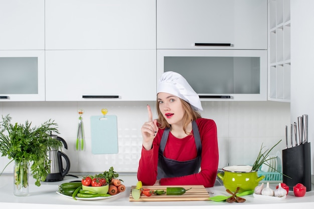 Бесплатное фото Вид спереди женский шеф-повар в шляпе повара, указывая пальцем вверх