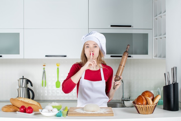 Front view female chef making hush sign holding rolling pin in the kitchen