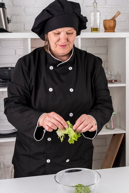 Front view of female chef tearing salad in bowl