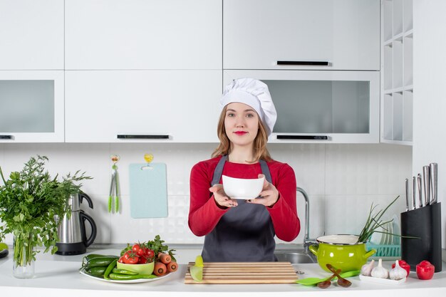 Front view female chef in uniform holding bowl in kitchen