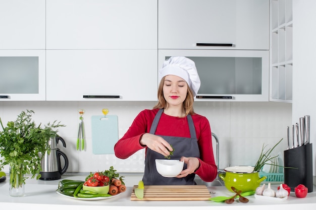 Front view female chef in uniform holding bowl with greens