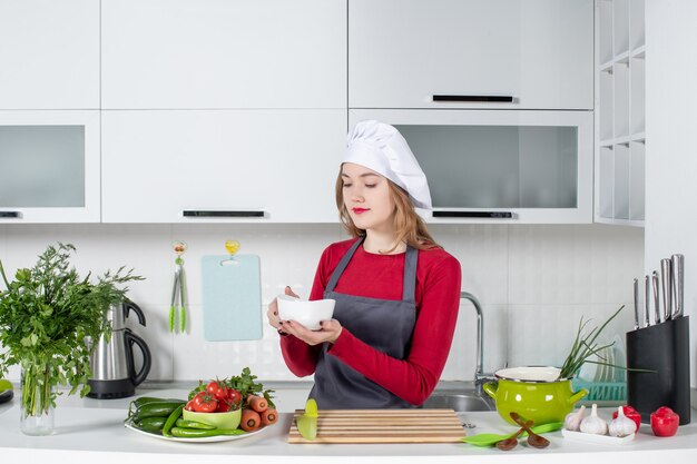 Вид спереди повар-женщина в униформе, стоящая за кухонным столом с миской