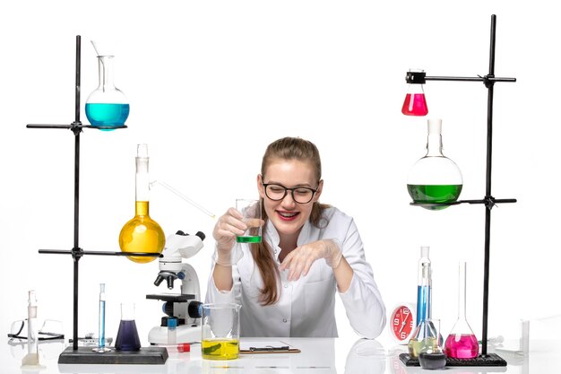 front view female chemist in medical suit checking smell of solution and laughing on white background chemistry pandemic health covid