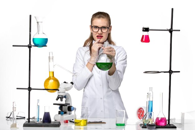 Front view female chemist in medical suit holding flask with green solution on a white background chemistry pandemic covid virus