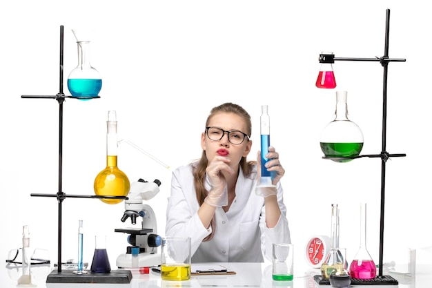 Front view female chemist in medical suit holding long flask with solution on light-white background chemistry pandemic health covid