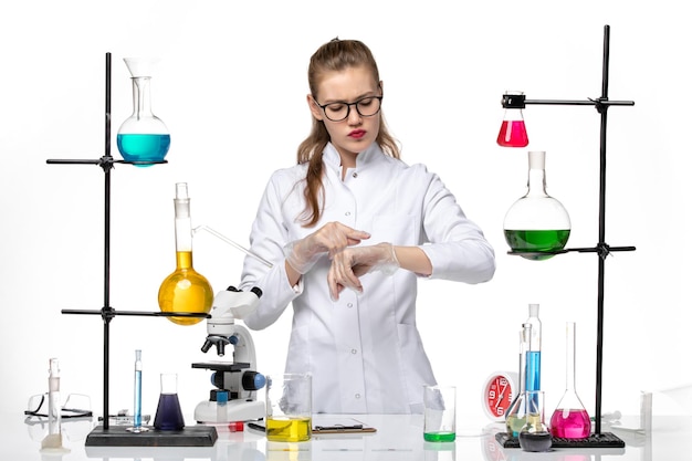 明るい白の背景の化学パンデミックコビッドウイルスで彼女の手首を見ている医療スーツの正面図の女性化学者