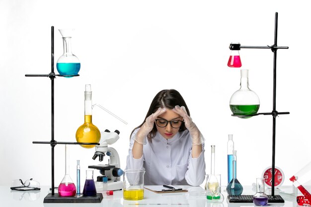 明るい白の背景ラボウイルスcovidパンデミック科学のソリューションとテーブルの周りに座っている医療スーツの正面図女性化学者