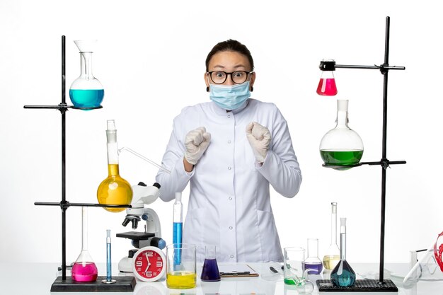 Front view female chemist in medical suit and wearing mask standing on a white background virus chemistry lab covid- splash