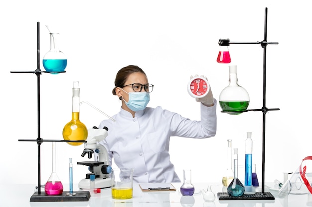 Front view female chemist in medical suit with mask holding clocks on white background virus lab chemistry covid splash