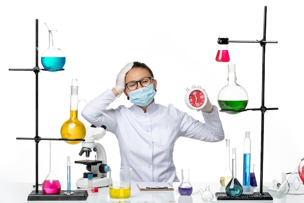 Вид спереди женщина-химик в медицинском костюме с маской, держащей часы на белом полу, вирусная лаборатория, химия, covid- splash