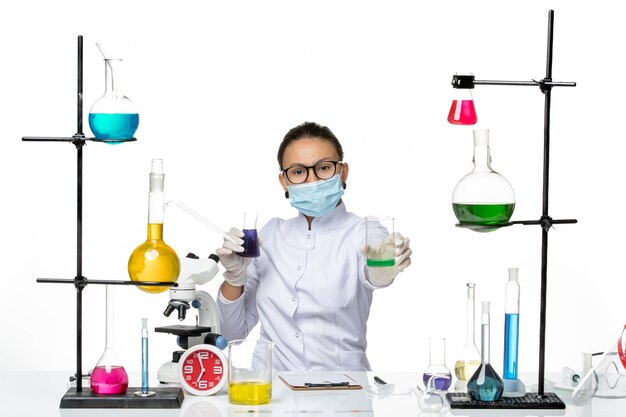 Front view female chemist in medical suit with mask holding different solutions on light-white background splash virus chemistry lab covid-