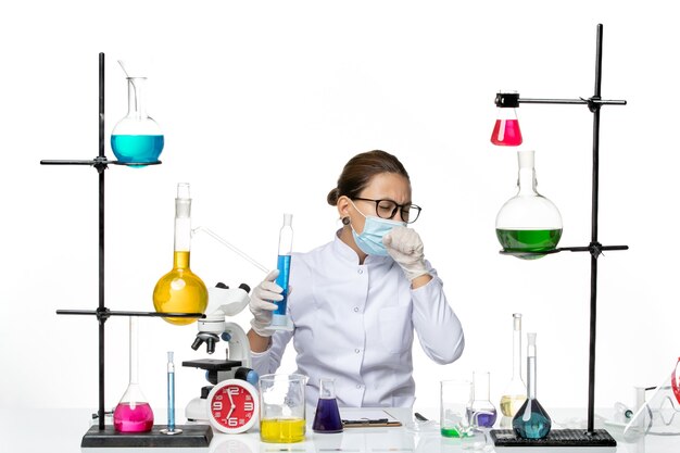 明るい白の背景に青い溶液とフラスコを保持しているマスクと医療スーツの正面図女性化学者スプラッシュウイルス化学実験室covid