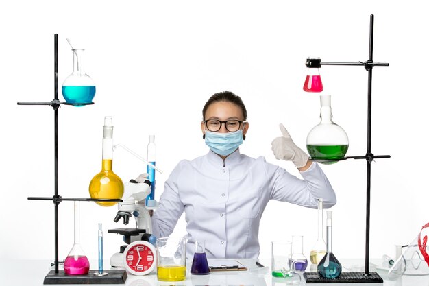 흰색 배경 스플래시 바이러스 화학 실험실 covid에 파란색 솔루션 미소와 플라스크를 들고 마스크와 의료 소송에서 전면보기 여성 화학자