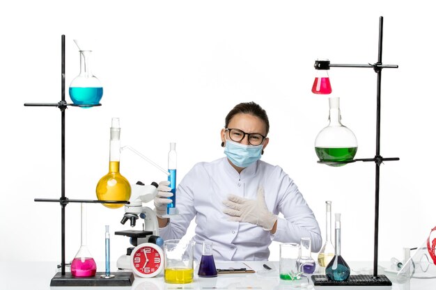 白い背景の上の青い溶液とフラスコを保持しているマスクと医療スーツの正面図女性化学者スプラッシュ化学実験室covid