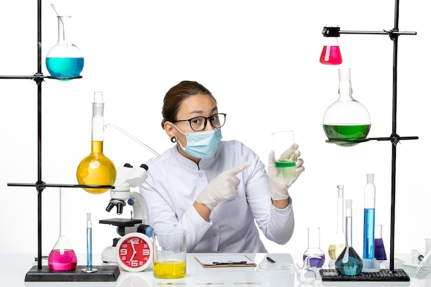 Вид спереди женщина-химик в медицинском костюме с маской, держащей зеленый раствор на белом фоне, всплеск лаборатории вирусной химии covid-