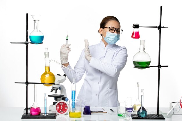 白い背景に注射を保持しているマスクと医療スーツの正面図女性化学者ウイルス化学実験室covidスプラッシュ