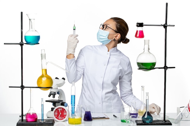 Вид спереди женщина-химик в медицинском костюме с маской, держащей инъекцию на белом фоне, вирусная химическая лаборатория, всплеск covid