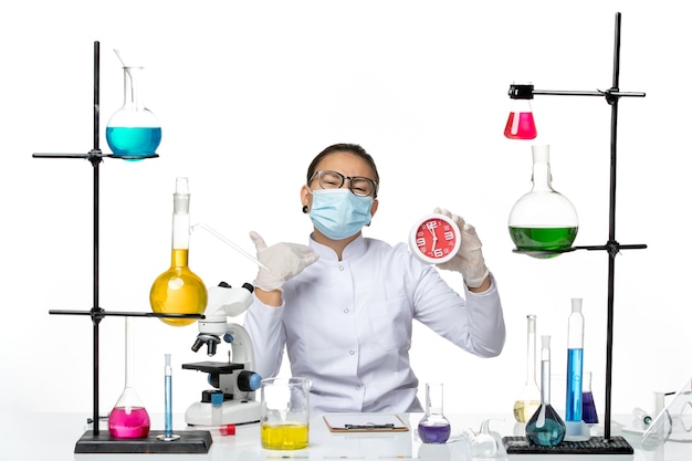 Front view female chemist in medical suit with mask holding red clocks on a white background splash virus chemistry covid- lab