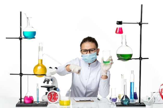 Front view female chemist in medical suit with mask holding solution on a light-white background splash lab virus chemistry covid-