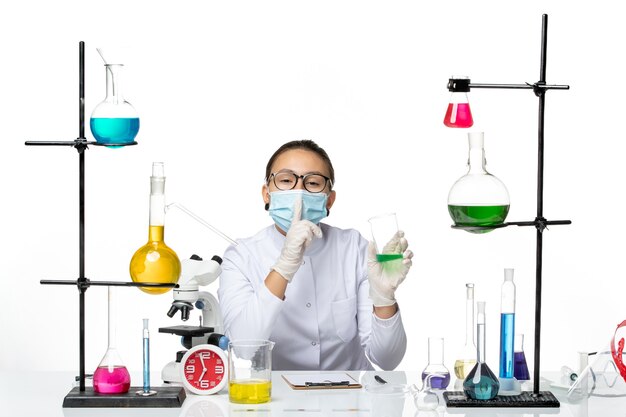 Front view female chemist in medical suit with mask holding solution on white desk splash lab virus chemistry covid-