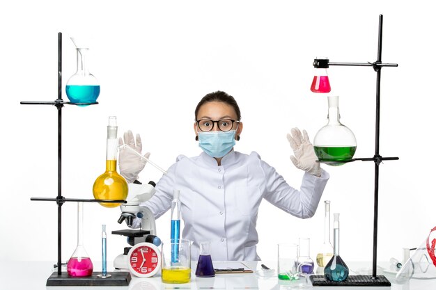 마스크는 흰색 배경에 솔루션 테이블 앞에 앉아 의료 소송에서 전면보기 여성 화학자 바이러스 화학 실험실 covid 시작