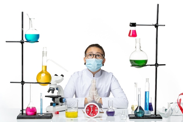 Front view female chemist in medical suit with mask sitting with solutions praying on white background virus lab chemistry covid splash