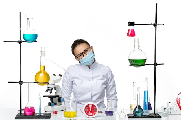 Front view female chemist in medical suit with mask sitting with solutions on white floor virus lab chemistry covid splash