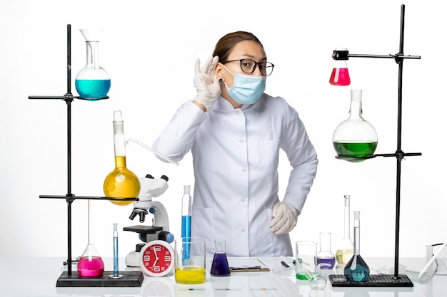 Front view female chemist in medical suit with mask trying to hear on white background virus chemistry lab covid- splash