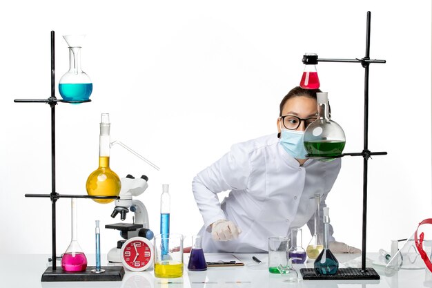 Front view female chemist in medical suit with mask working with solutions on the white background virus chemistry lab covid splash