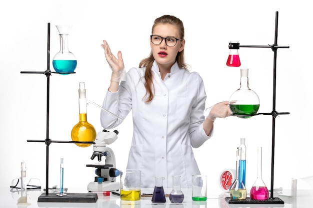 Front view female chemist in medical suit working with different solutions on light white background chemistry pandemic covid- virus