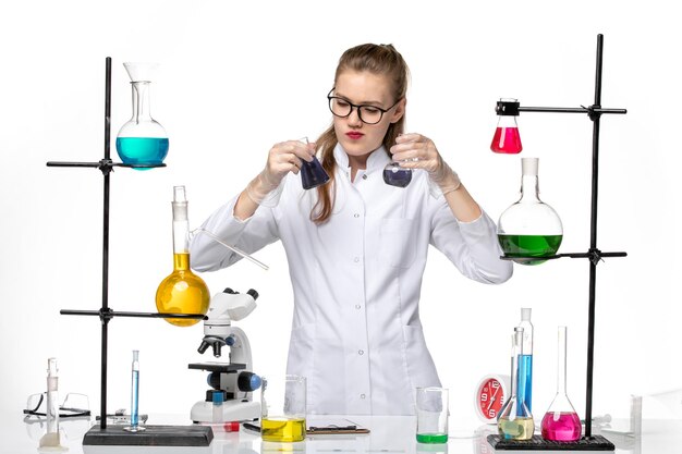 Front view female chemist in medical suit working with different solutions on a white background chemistry pandemic covid- virus