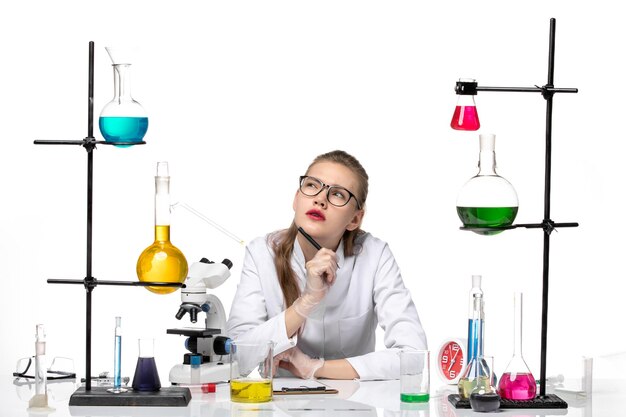 Front view female chemist in medical suit writing notes and thinking on white background chemistry pandemic health covid