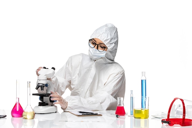 흰색 배경 화학 covid- 건강 바이러스에 현미경으로 샘플을 검사하는 특수 보호 복의 전면보기 여성 화학자