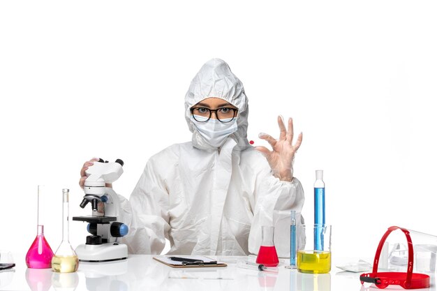 흰색 배경에 현미경으로 샘플을 검사하는 특수 보호 복의 전면보기 여성 화학자 화학 covid 바이러스 전염병