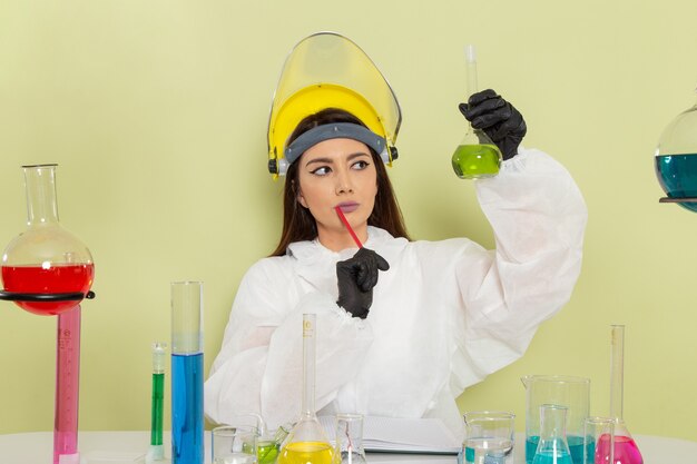 Front view female chemist in special protective suit in front of table with solutions working with them on green surface
