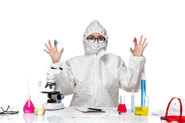 Front view female chemist in special protective suit holding empty flasks on light white background virus health chemistry covid