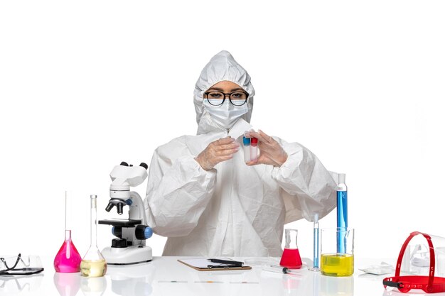 Front view female chemist in special protective suit holding empty flasks on the white background health virus chemistry covid