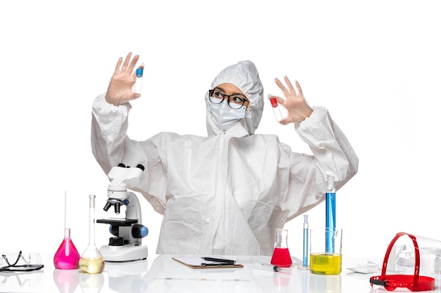 Front view female chemist in special protective suit holding empty flasks on a white background virus health chemistry covid