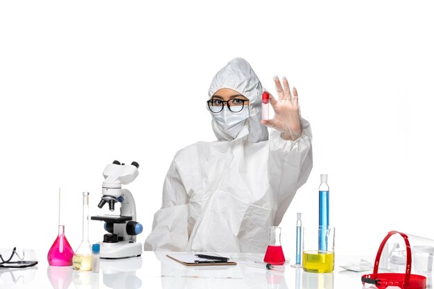 Front view female chemist in special protective suit holding flask on white desk virus health chemistry covid-