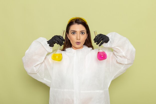 Front view female chemist in special protective suit holding flasks with solutions on light green surface