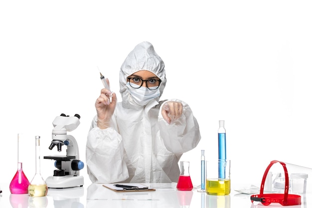 Вид спереди женщина-химик в специальном защитном костюме, держащая инъекцию на белом фоне, пандемия химического вируса ковид-вируса