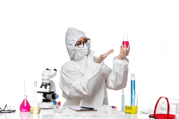 明るい白の背景に赤い溶液を保持している特別な防護服を着た女性化学者の正面図covid-chemistryvirus lab