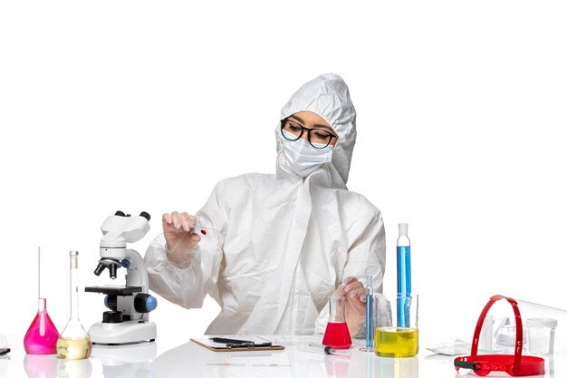 Вид спереди женщина-химик в специальном защитном костюме держит образец на белом столе, пандемия вируса химии ковид