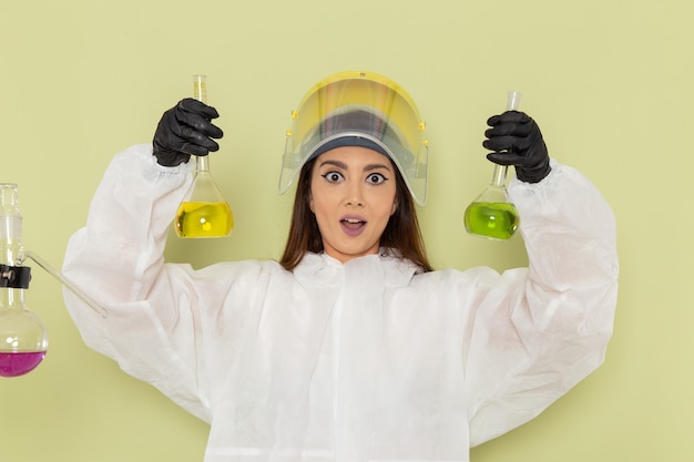 Free photo front view female chemist in special protective suit holding with different solutions on green surface