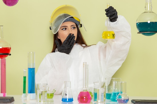 Front view female chemist in special protective suit holding yellow solution on green surface