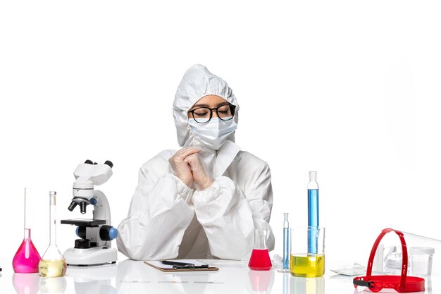 Front view female chemist in special protective suit sitting with solutions on light white background chemistry covid- virus pandemic