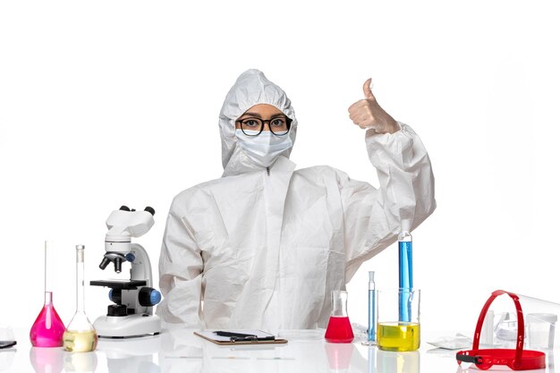 ライトホワイトの背景化学covidウイルスパンデミックのソリューションと一緒に座っている特別な防護服の正面図女性化学者