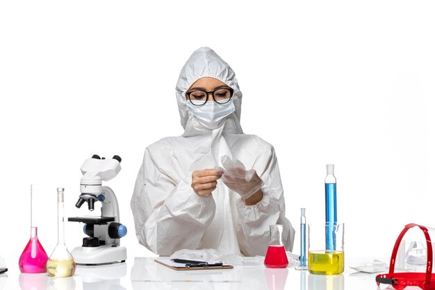 Front view female chemist in special protective suit sitting with solutions on white background chemistry pandemic covid- virus